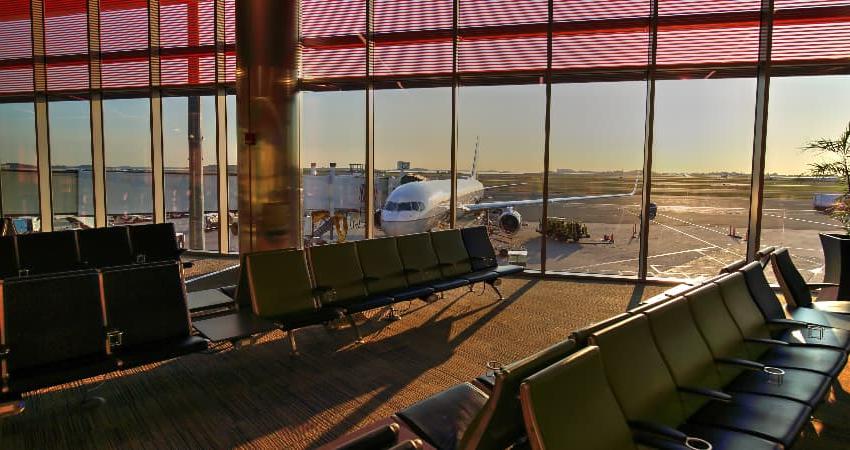 The sun rises over an empty gate at Boston Logan International Airport, a passenger plane visible outside the floor-to-ceiling windows