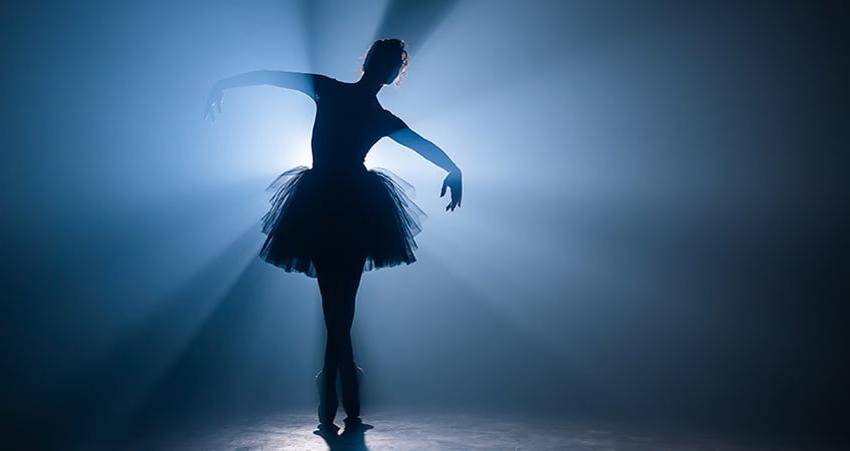 A ballet dancer poses on a dimly lit stage